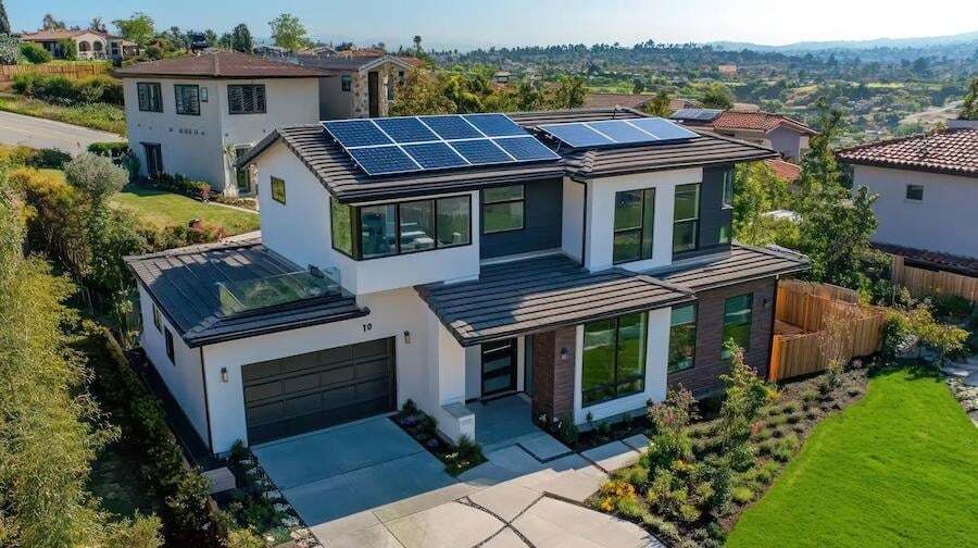 Modern two-story house with solar panels on the roof, a two-car garage, landscaped yard, and surrounded by other homes in a suburban neighborhood.